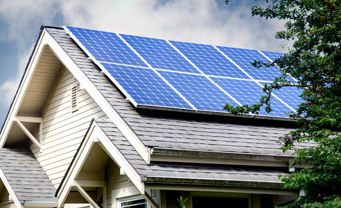 A house with blue solar panels across its roof under a cloudy sky